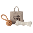 A beige fabric tote labeled “Goodie Bag” with a dog illustration is flanked by a knotted rope toy on the left and a plush bone toy on the right, set against a white background.