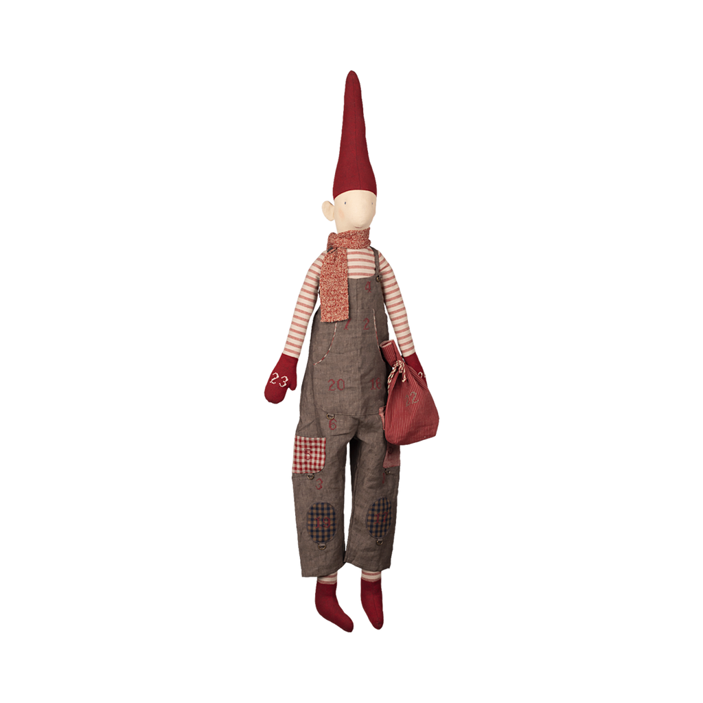 A whimsical fabric doll with a tall red hat, striped shirt, gray overalls, scarf, mittens, and boots, holding a red bag. The tone is playful and festive.