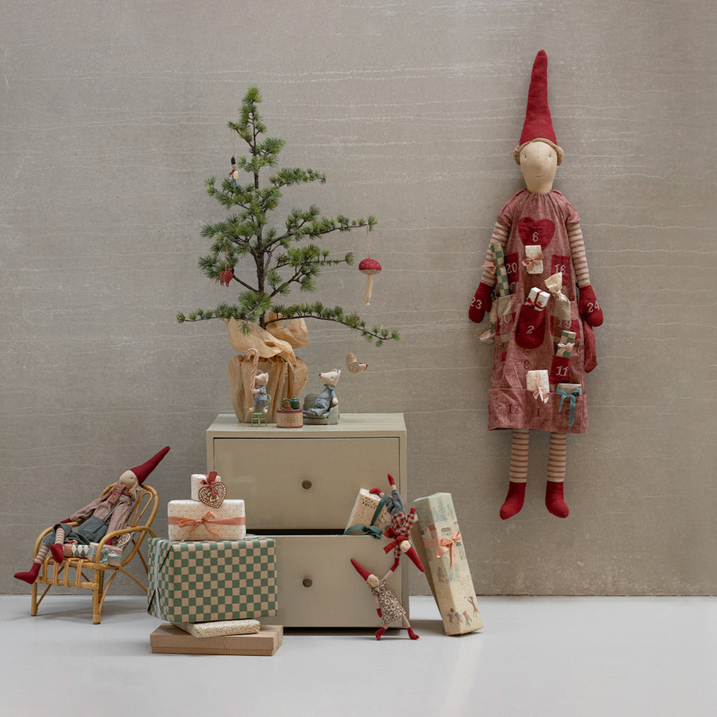 Whimsical Christmas scene with a small tree, gifts, and playful elf dolls. A fabric doll wearing a calendar dress adds festive charm and warmth.