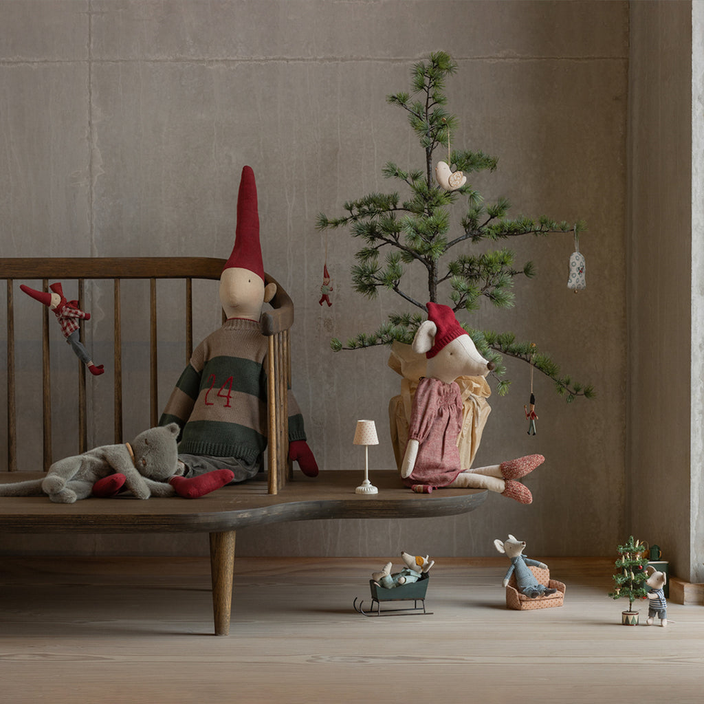 Cozy scene with dolls: A fabric elf doll and plush bear sit on a wooden bench beside a small, decorated Christmas tree. Mice dolls in winter attire are nearby, creating a whimsical, festive atmosphere.