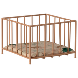 A small, beige metal playpen with vertical bars stands on a white background. Inside is a cushioned mat featuring a subtle floral pattern in green and pink tones.