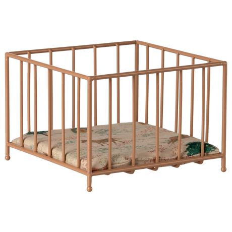 A small, beige metal playpen with vertical bars stands on a white background. Inside is a cushioned mat featuring a subtle floral pattern in green and pink tones.