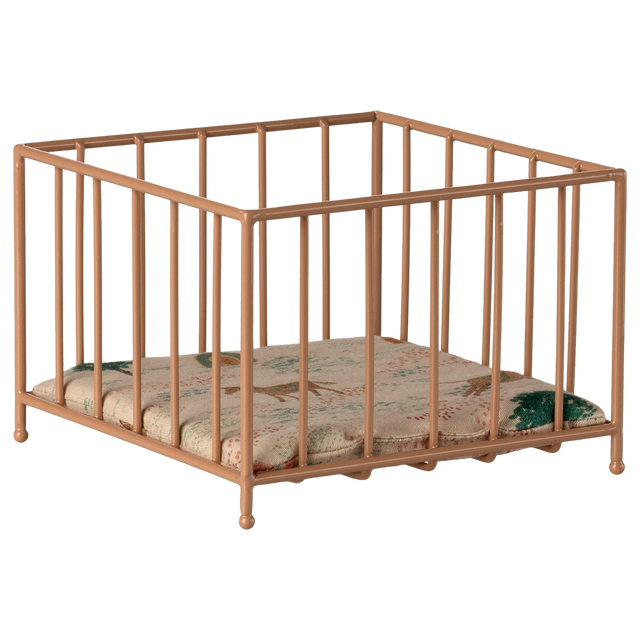 A small, beige metal playpen with vertical bars stands on a white background. Inside is a cushioned mat featuring a subtle floral pattern in green and pink tones.