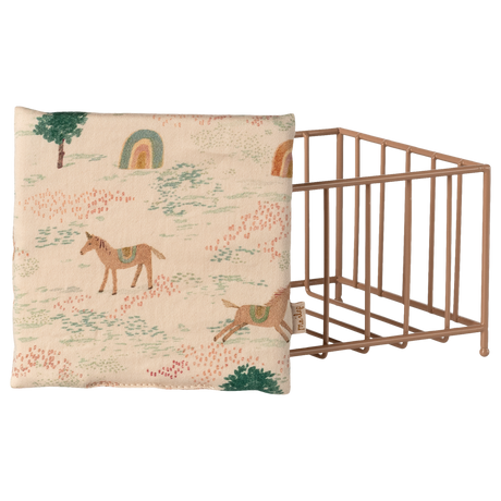 Fabric with a whimsical pattern of horses, trees, and rainbows on a beige background. A pink metal wire grid crate is partially visible on the right.