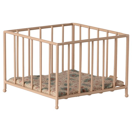 A small, beige metal playpen with a colorful, quilted cushion sits empty against a white background, conveying a sense of simplicity and nostalgia.