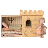 Toy set depicting "The Princess and the Pea" with a plush mouse in a patterned dress beside a castle box. Inside, layered mattresses are under a chandelier.