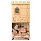 A toy mouse in a pink dress lies atop a stack of colorful fabric mattresses inside a box resembling a castle. A window illustration shows a mouse peeking out. The text reads "The Princess Mouse and the pea."