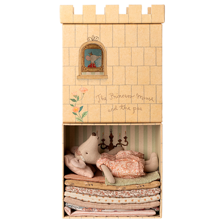 A toy mouse in a pink dress lies atop a stack of colorful fabric mattresses inside a box resembling a castle. A window illustration shows a mouse peeking out. The text reads "The Princess Mouse and the pea."