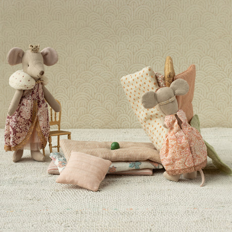 Plush mice in royal clothing stand beside a stack of bedding, including soft pastel cushions and a visible pea, illustrating "The Princess and the Pea."