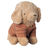 A plush beige puppy wearing a snug, striped brown knit sweater sits against a white background, radiating a cozy and endearing charm.