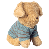 A fluffy, light brown teddy bear wears a blue, knitted sweater with brown stripes. Its expression is calm and endearing, against a white background.