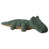A soft, plush, green crocodile toy with a tan underside lies flat. The toy has a simple, friendly design, creating a playful and calming tone.