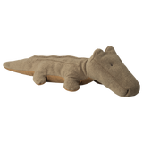 A brown, plush alligator toy is shown on a white background. The design is simple and cute, with small eyes and soft texture, conveying a playful tone.