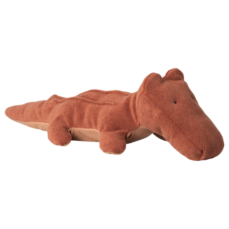 A brown plush crocodile toy lies on a white background. The toy has a soft, textured surface with a whimsical, friendly expression, conveying a playful mood.