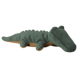 A soft, plush crocodile toy lies against a white background. The toy is dark green with a brown underside, featuring simple, stitched details.
