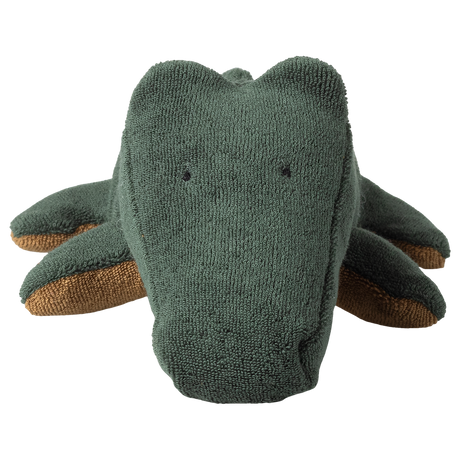A plush crocodile toy with a textured, dark green surface and small, sewn eyes and smile. Its brown underbelly is visible. The image has a playful tone.