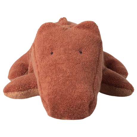 Brown plush crocodile toy with simple black eyes on a plain white background, conveying a cute and cuddly appearance.