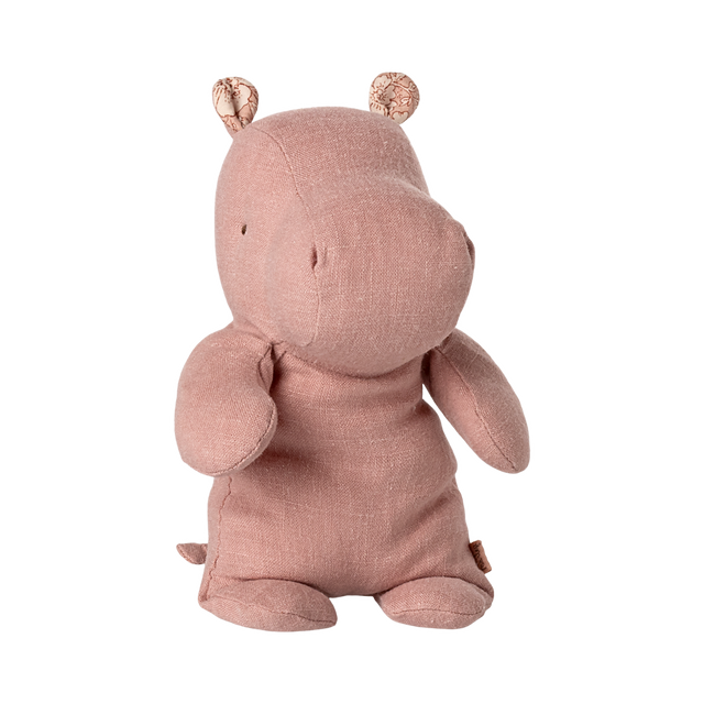 A soft, pink hippo plush toy with small round ears and stitched details sits upright against a plain background, conveying a cute and cuddly vibe.