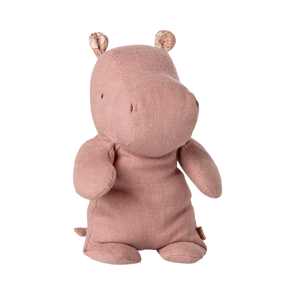 A soft, pink hippo plush toy with small round ears and stitched details sits upright against a plain background, conveying a cute and cuddly vibe.