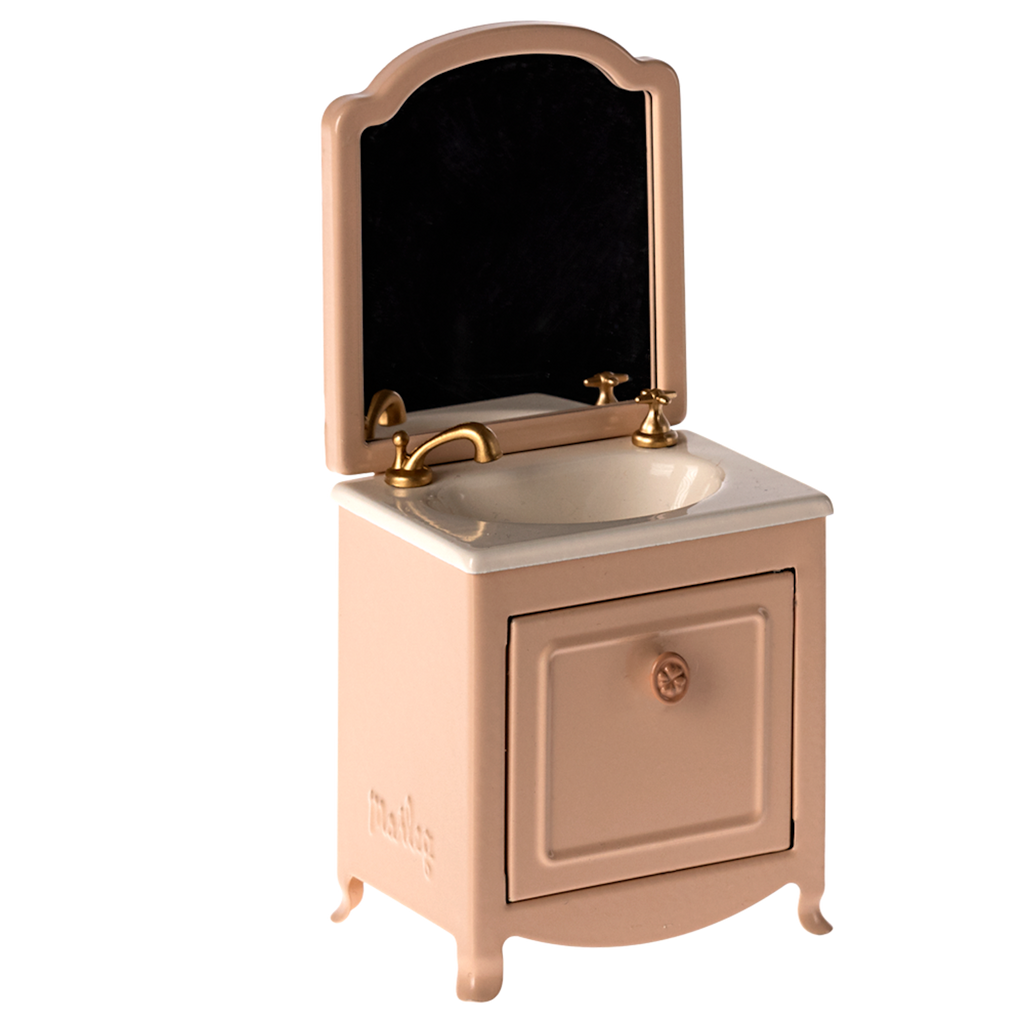 Miniature pink bathroom vanity with a small cabinet, white sink, gold-toned faucet, and mirror. Background is white, highlighting its vintage style.
