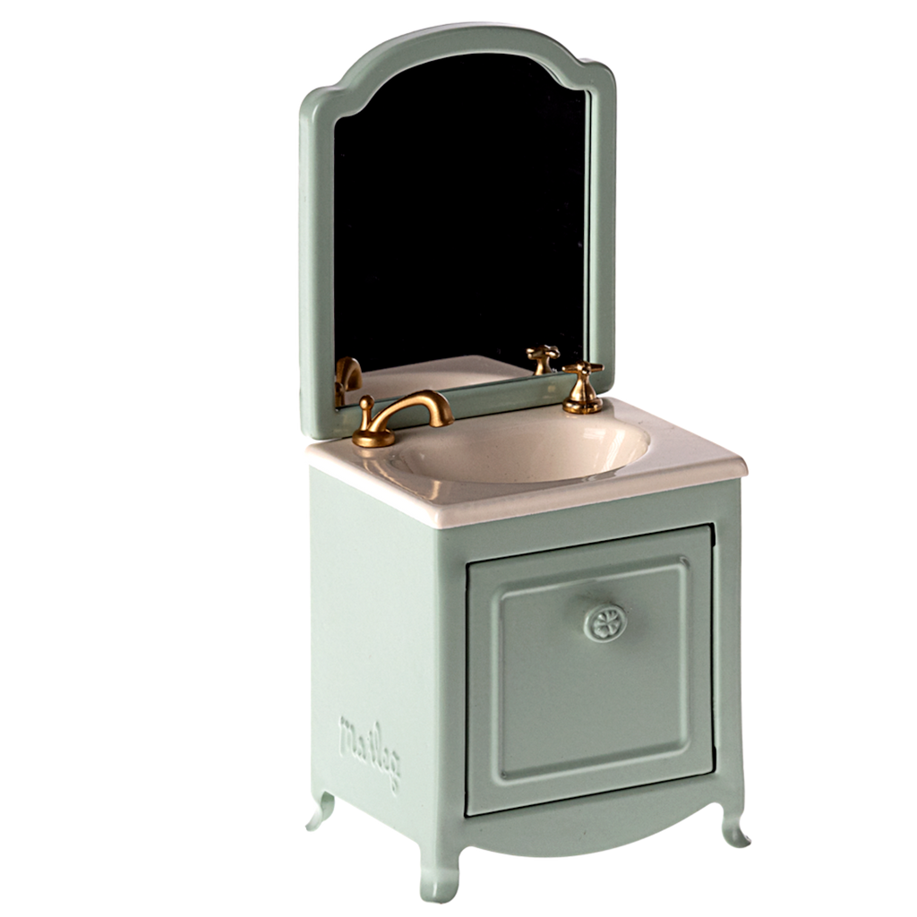 A miniature vanity features a light green cabinet with a white basin and gold faucet. It has an arched mirror, set against a white background.