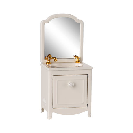 A miniature white vanity with a mirror, featuring a gold faucet and taps. The cabinet door is slightly ajar, conveying a quaint and elegant feel.