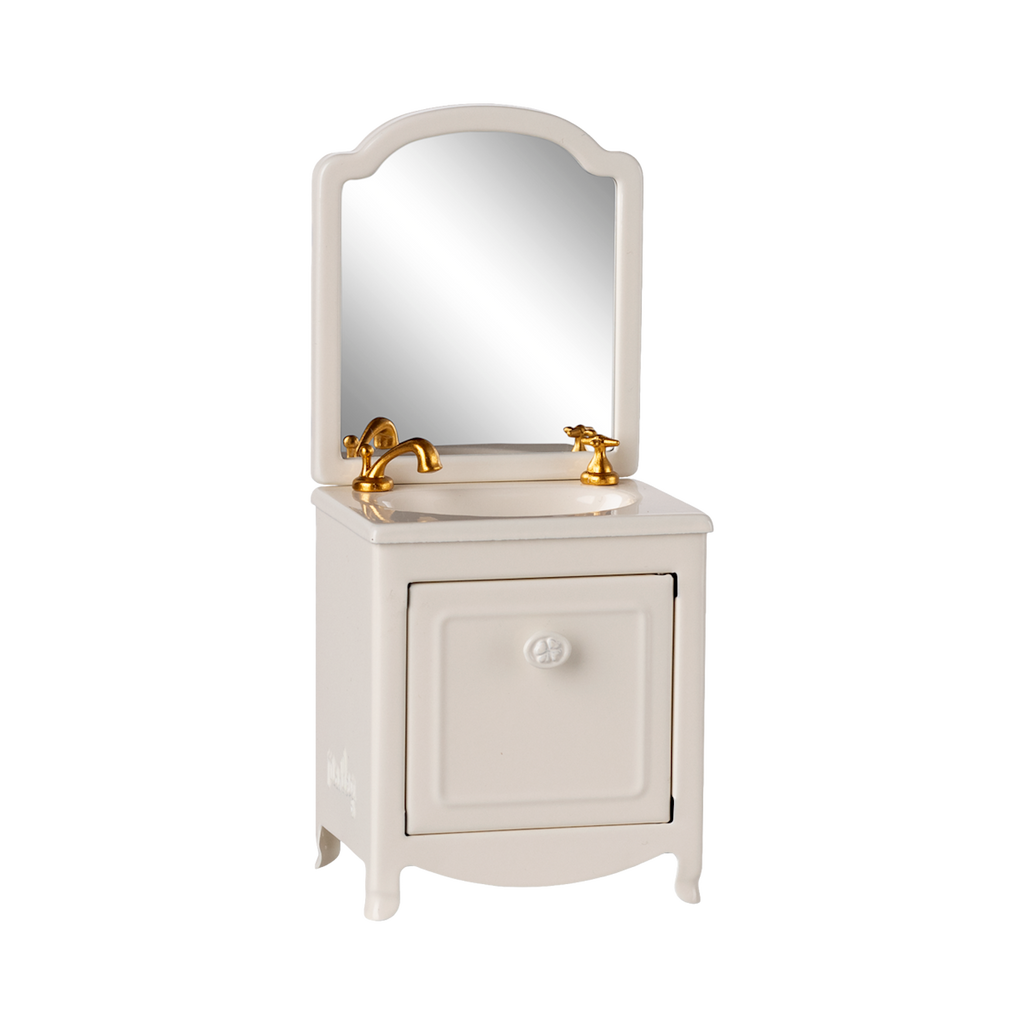 A miniature white vanity with a mirror, featuring a gold faucet and taps. The cabinet door is slightly ajar, conveying a quaint and elegant feel.