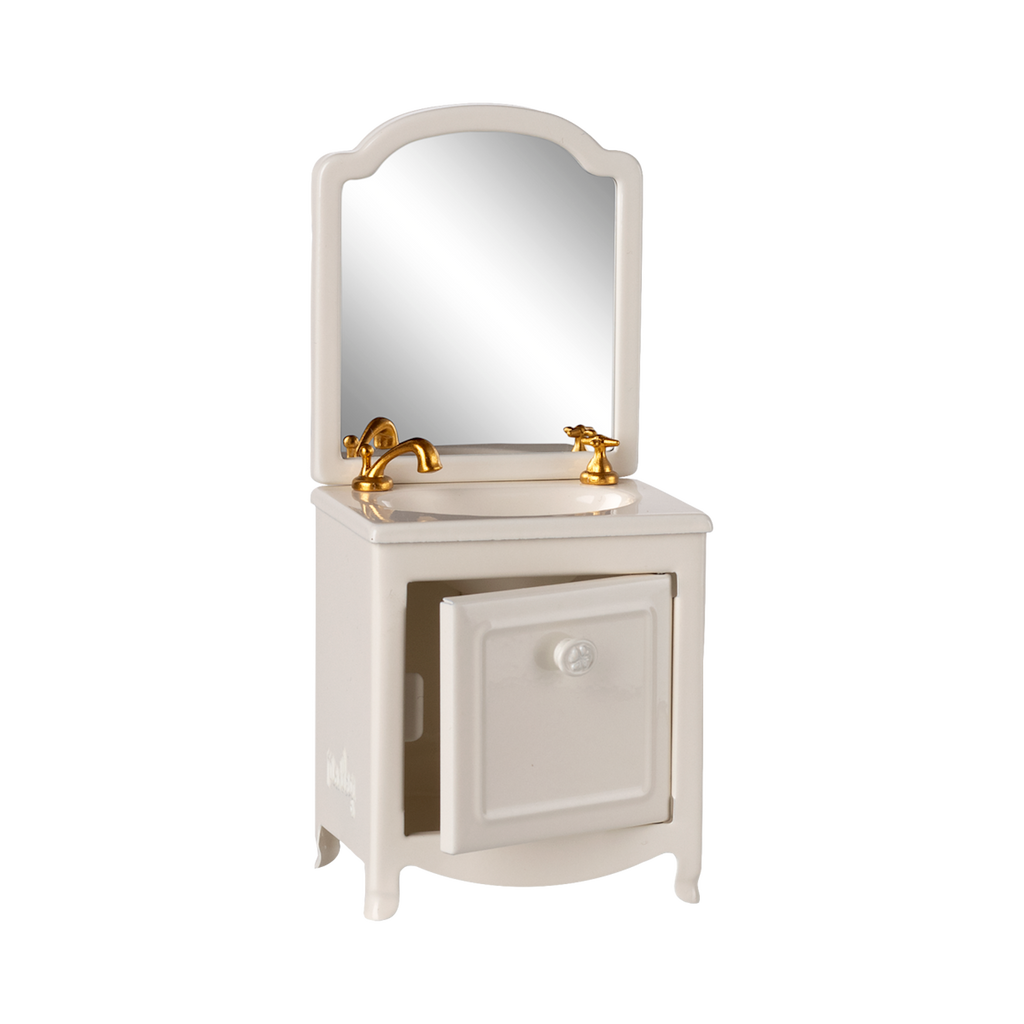 A miniature white vanity with a mirror, featuring a gold faucet and taps. The cabinet door is slightly ajar, conveying a quaint and elegant feel.