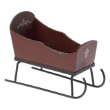 Brown wooden sled with decorative white patterns on the sides, set on black metal runners against a white background. It has a rustic, vintage feel.