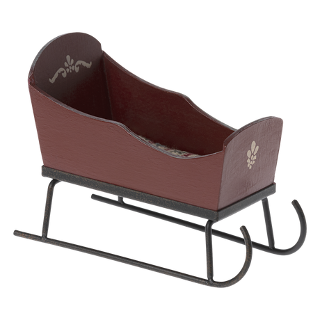 Brown wooden sled with decorative white patterns on the sides, set on black metal runners against a white background. It has a rustic, vintage feel.