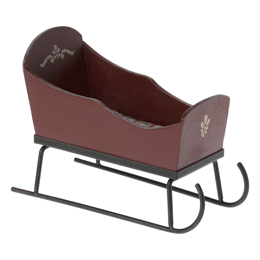 Brown wooden sled with decorative white patterns on the sides, set on black metal runners against a white background. It has a rustic, vintage feel.