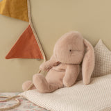 Maileg small bunny plush in powder pink sitting on a polka dot pillow with decorative bunting in a nursery.