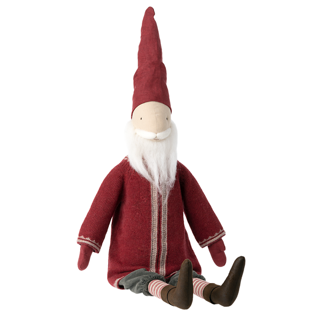 A whimsical gnome toy sits with a long red hat, white beard, red robe, and brown boots. Its cheerful demeanor evokes a festive, playful tone.