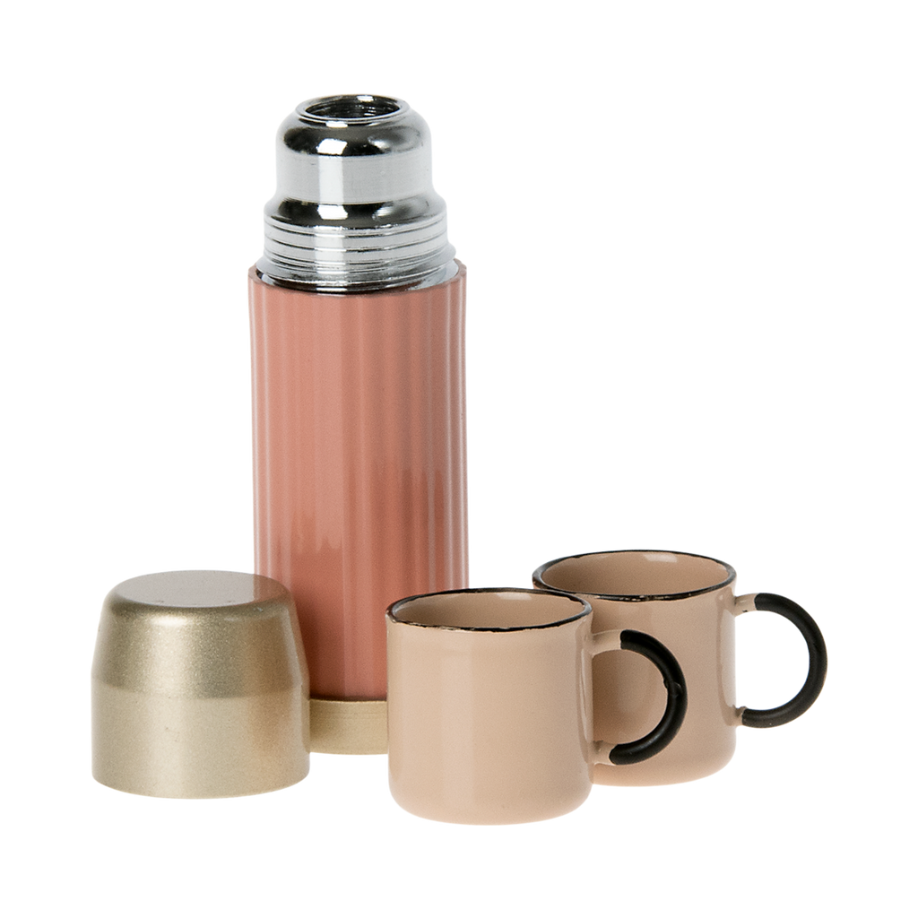 A stylish pink thermos with a gold lid and two matching pastel cups in white background.