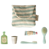 A striped pouch alongside a green shampoo bottle, a white cup, a blue toothpaste tube, a toothbrush, and a hairbrush, arranged on a white background.