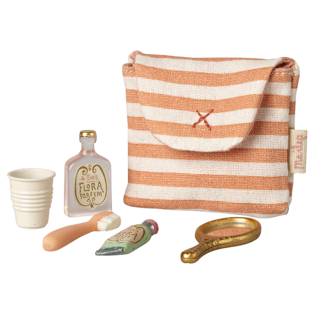 A small striped fabric pouch with a red cross is surrounded by a collection of miniature toiletries: a white cup, a perfume bottle, a toothbrush, a toothpaste tube, and a golden hand mirror, all against a white  background.