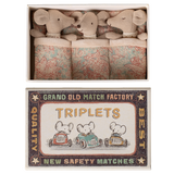 A matchbox labeled "Triplets" contains three plush mice cuddled in patterned blankets, exuding a cozy and whimsical tone.
