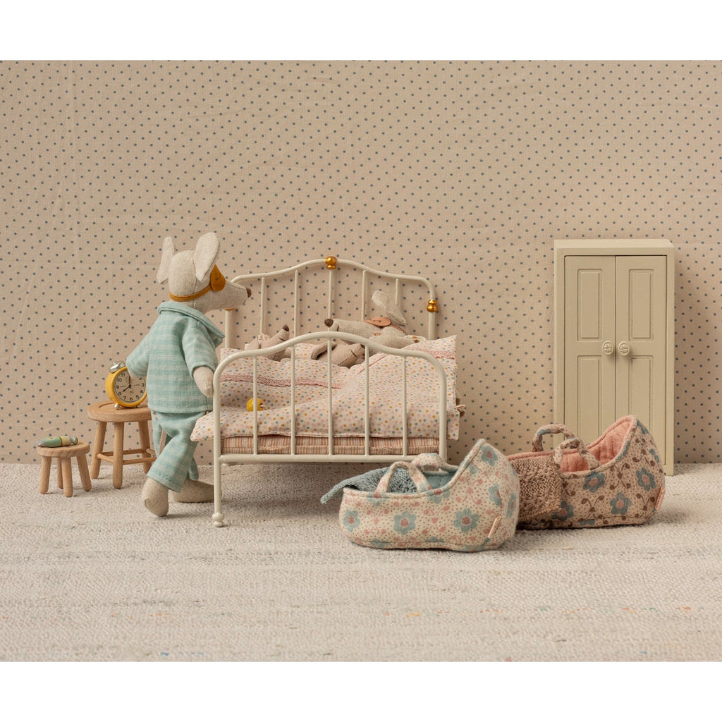 Antique-style miniature white metal bed with curved headboard and footboard, adorned with golden accents. Covered in polka-dot bedding and ruffled pillow.