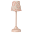 A vintage-style table lamp with a soft pink base and stem. The lampshade features a light blue fabric with intricate red floral patterns, set against a white background.
