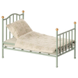 A miniature, vintage-style metal bed with a pale green frame and golden accents. It has a cream-colored, patterned quilt and pillow, conveying a nostalgic charm.