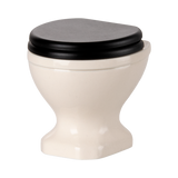 A miniature, white ceramic toilet with a black seat and lid open, set against a plain black background, conveying a quirky and playful tone.