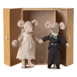 Two stuffed mice dressed as a bride and groom stand inside an ornate, open box. The bride holds a bouquet, and the groom wears a bow tie.