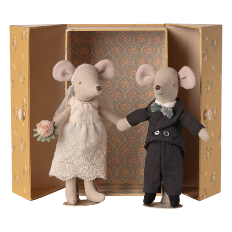 Two stuffed mice dressed as a bride and groom stand inside an ornate, open box. The bride holds a bouquet, and the groom wears a bow tie.