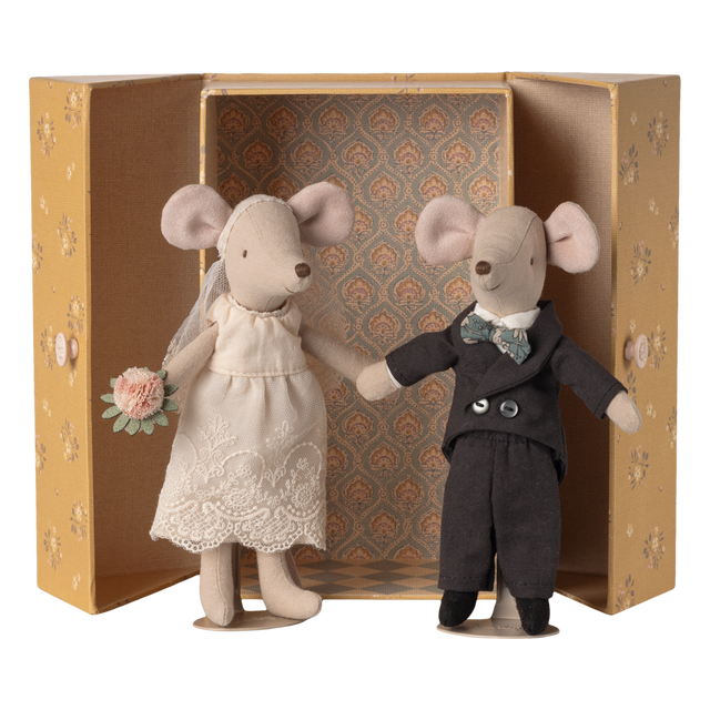 Two stuffed mice dressed as a bride and groom stand inside an ornate, open box. The bride holds a bouquet, and the groom wears a bow tie.