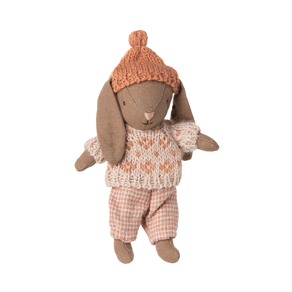 A handmade rabbit doll wearing a knitted orange hat and cozy sweater, with checkered pants, exuding a gentle, vintage charm.