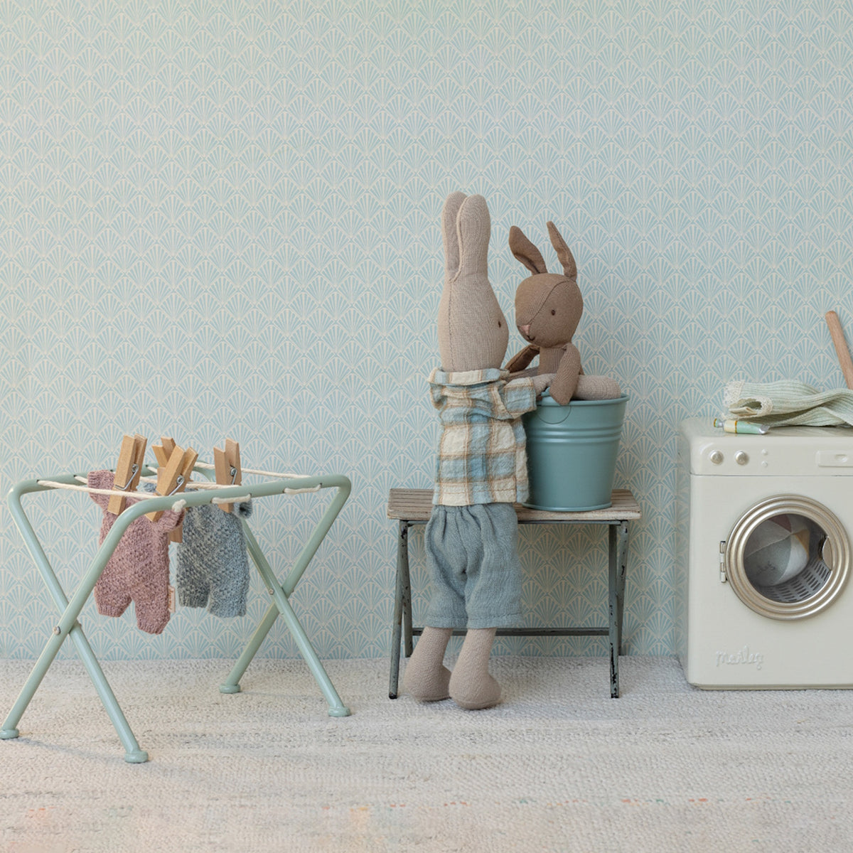 Maileg micro rabbits doing laundry with a miniature washing machine, drying rack, and blue bucket.