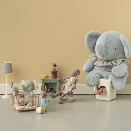 Maileg plush rabbits and elephants in a miniature playroom with a toy crib, rocking chair, and washing machine.