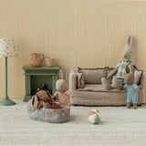 Maileg micro rabbits in a miniature living room with a sofa, fireplace, and dollhouse furniture.