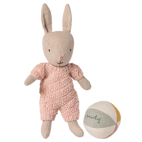 Maileg micro rabbit wearing a pink knitted suit standing next to a small fabric ball on a white background.