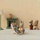 Maileg micro rabbits playing in a dollhouse room with a bouncer, ball, and watering can.